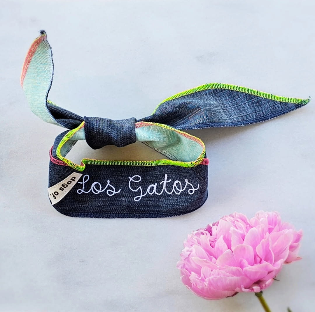 Local denim dog scarf tie with colorful accents and 'Los Gatos' embroidery on a light background with a pink flower.