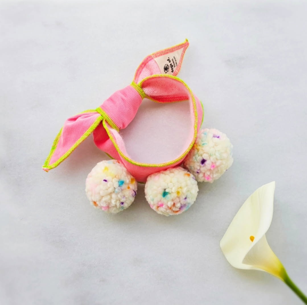 Pink dog scarf tie with colorful pom-poms on a light background